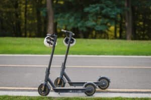 2 trottinettes sont présentées sur le bord de la route. Parmi les meilleures marques de pièces détachées pour trottinettes électriques, Xiaomi.