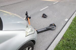 Après un accident avec une voiture, une trottinette cassée reste au sol.