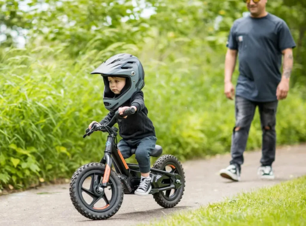 Un enfant fait de la draisienne électrique enfant avec son père dans un parc.