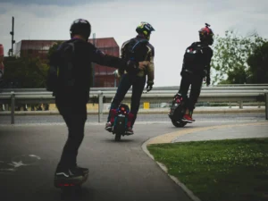 Un homme circule en monoroue électrique sur un chemin goudronné suivi de près par d'autres usagers de monoroues.