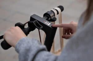 Une jeune femme tente de comprendre comment réparer sa trottinette électrique en appuyant longuement sur le bouton de démarrage.