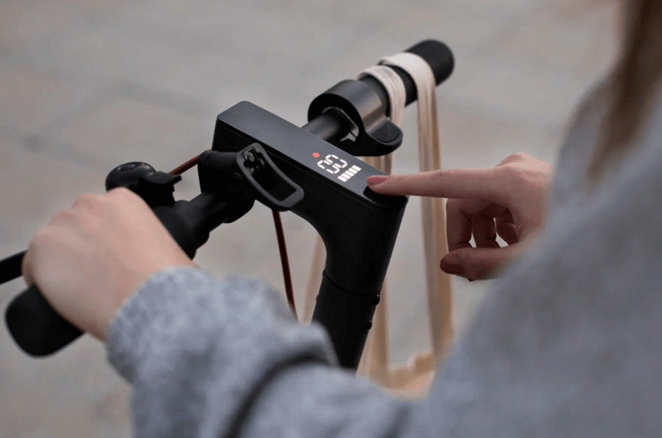 Une jeune femme tente de comprendre comment réparer sa trottinette électrique en appuyant longuement sur le bouton de démarrage.