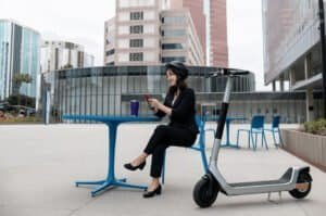 Une femme assise sur une chaise sur le parvis de son entreprise est allée au travail en trottinette électrique.