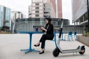 Une femme assise sur une chaise sur le parvis de son entreprise est allée au travail en trottinette électrique.