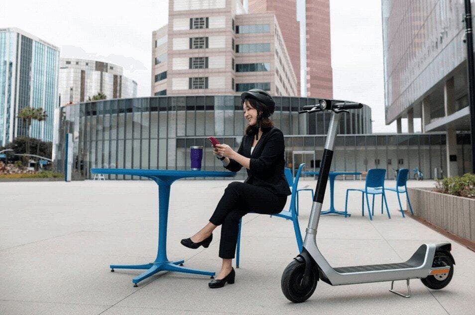 Une femme assise sur une chaise sur le parvis de son entreprise est allée au travail en trottinette électrique.