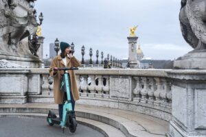 Une jeune femme se tient sur le pont Alexandre III, elle utilise une trottinettes en libre-service à Paris.